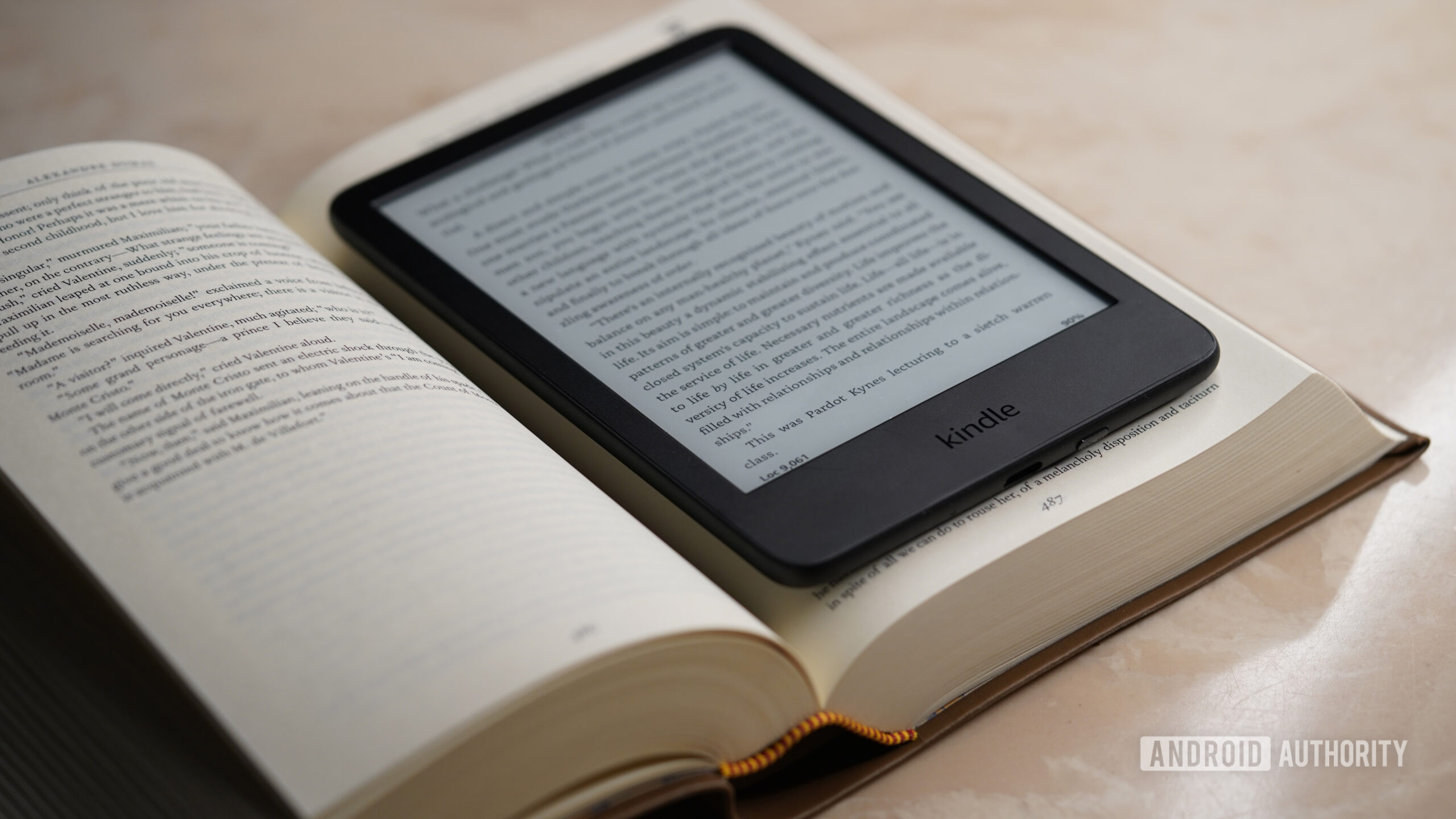 A Kindle rests on the pages of an open print book.