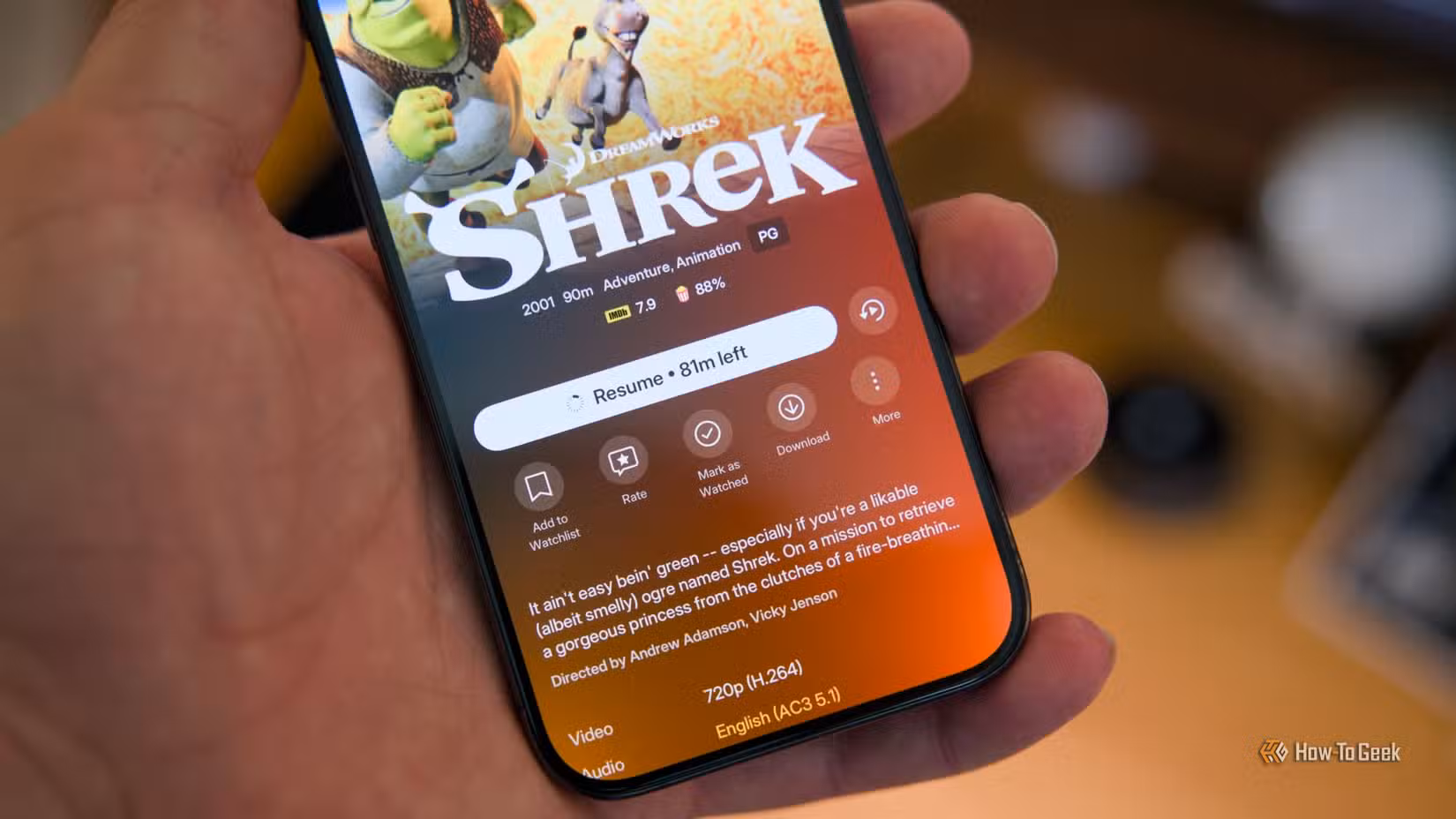 Um iPhone 15 Pro na mão mostrando o aplicativo móvel Plex com o ícone de download visível no filme Shrek.